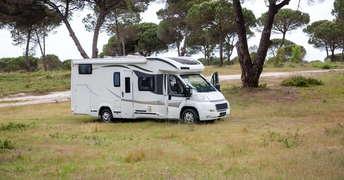 Impactante fotografía de una autocaravana en un campo sereno en Portugal, rodeada de árboles.