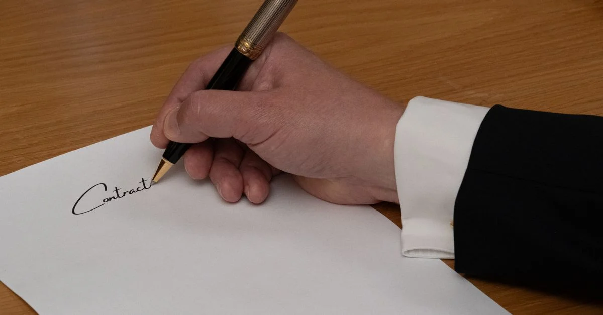 Un profesional firma un contrato comercial con una pluma estilográfica sobre un escritorio de madera.