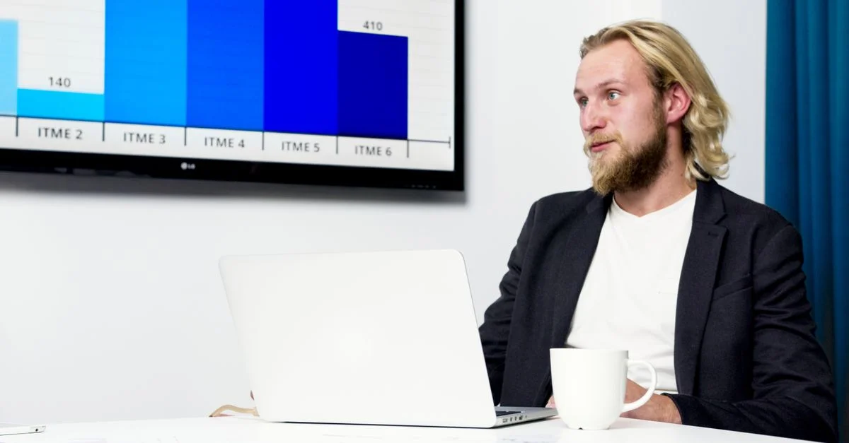 Empresario en una reunión analizando datos en un portátil con un gráfico en la pantalla.
