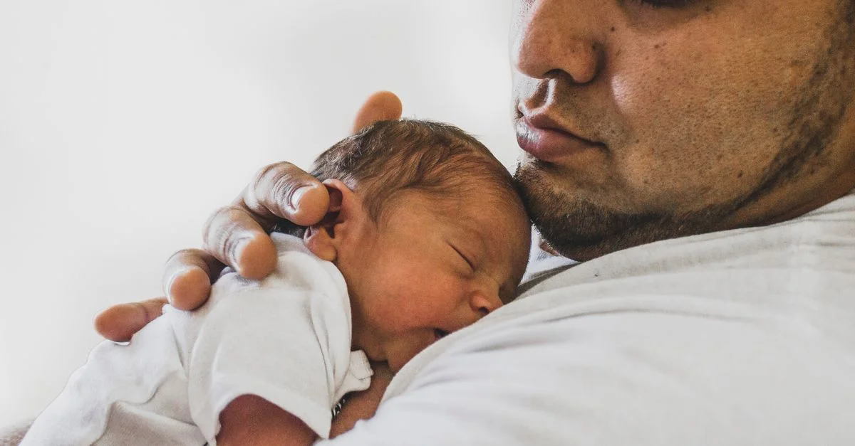 Una escena conmovedora de un padre sosteniendo suavemente a su bebé recién nacido dormido, mostrando amor y conexión familiar.