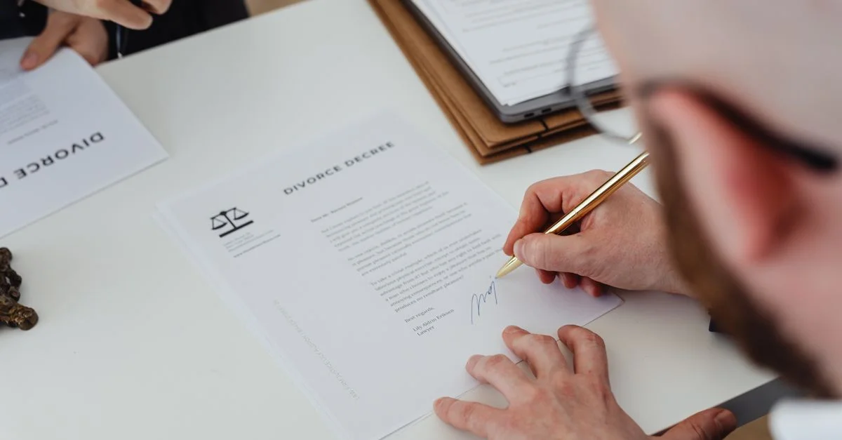 Primer plano de una persona firmando un decreto de divorcio sobre un escritorio.