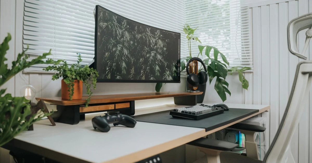 Un elegante espacio de oficina en casa con un monitor curvo, teclado y plantas verdes.