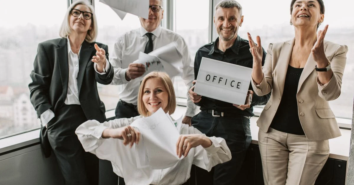 Un grupo diverso de profesionales de negocios celebrando alegremente en un entorno de oficina, simbolizando el trabajo en equipo.