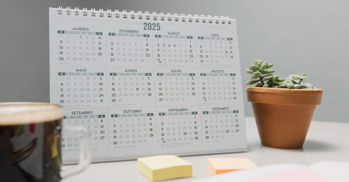 Un calendario de escritorio 2025 con café, notas adhesivas y suculentas para planificar.