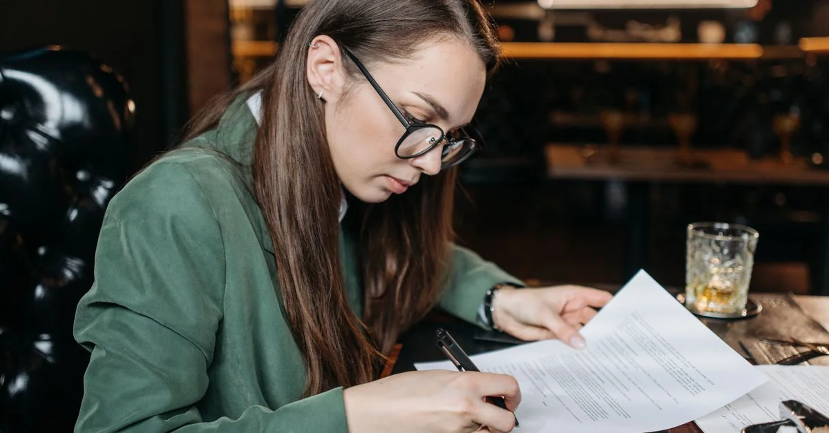 Mujer de negocios enfocada en atuendo verde firmando documentos importantes en su escritorio.