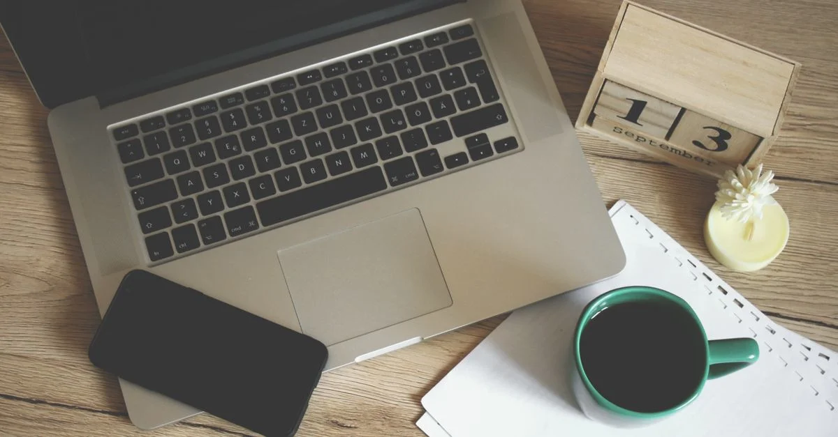 Configuración de oficina moderna con laptop, smartphone, café y calendario para un entorno de trabajo productivo.