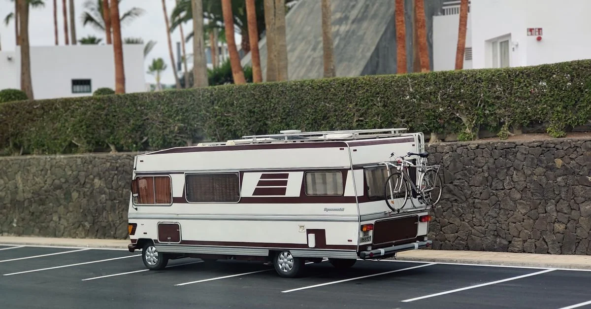 Una autocaravana vintage estacionada al aire libre cerca de un edificio moderno con palmeras, lo que sugiere una mezcla de aventura y relajación.