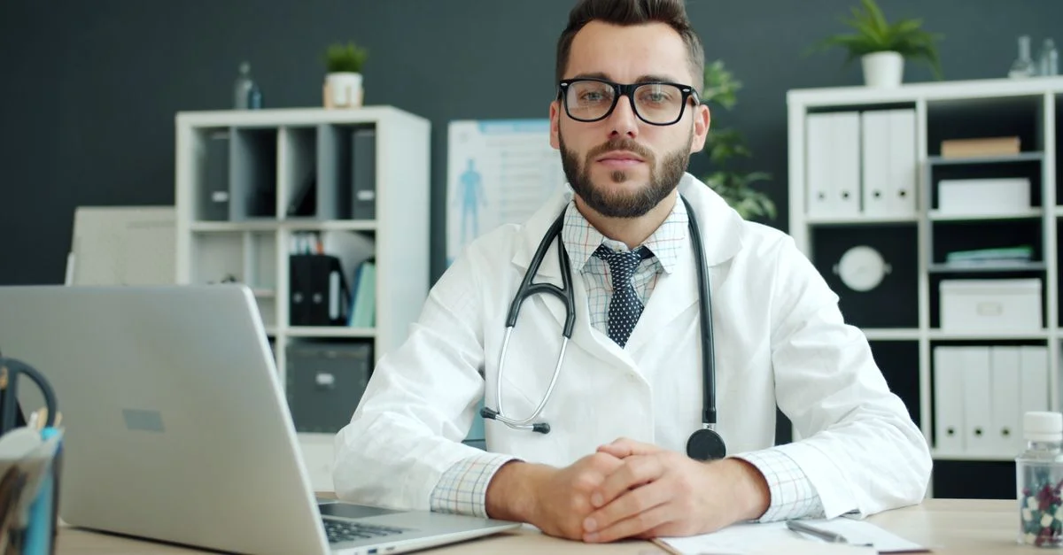 Médico varón con estetoscopio en su escritorio, seguro de sí mismo y profesional.