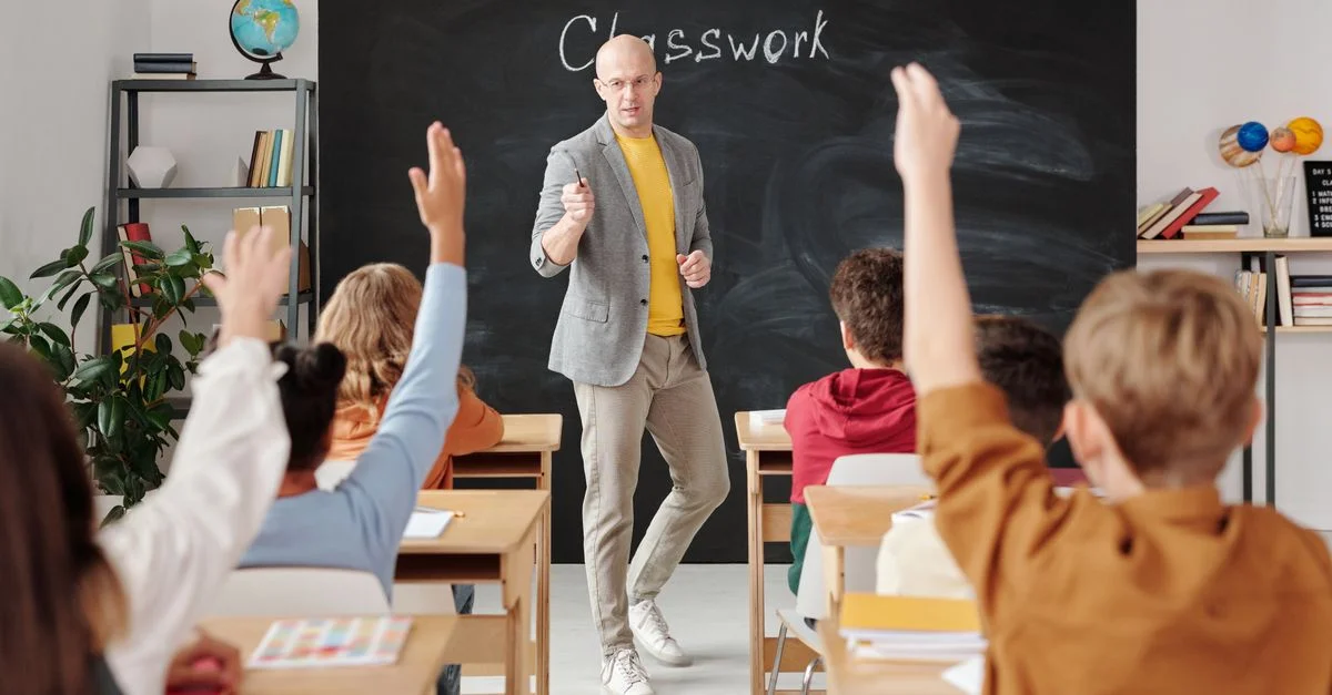 Profesor interactuando con estudiantes que levantan la mano en un aula.