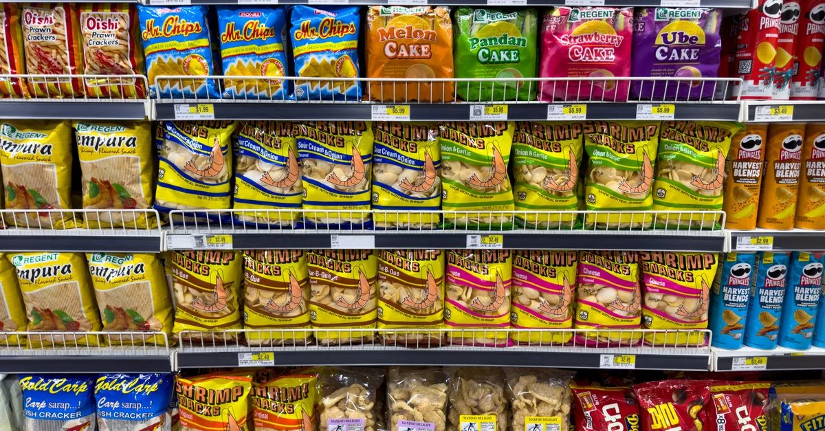 Paquetes de snacks coloridos exhibidos ordenadamente en un pasillo de supermercado, mostrando variedad de comida asiática.