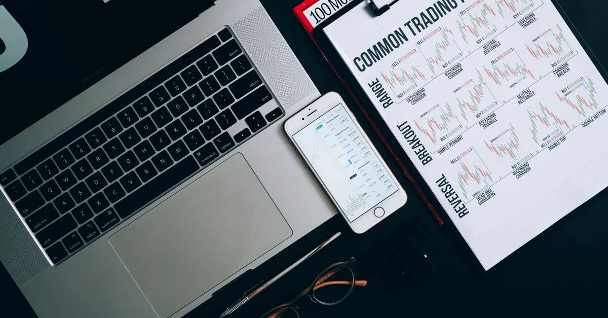 Una composición de flat lay que presenta un laptop, smartphone y gráficos de patrones de trading para análisis financiero.