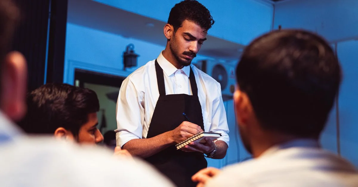Un atento camarero anota el pedido de un cliente en un acogedor restaurante interior.