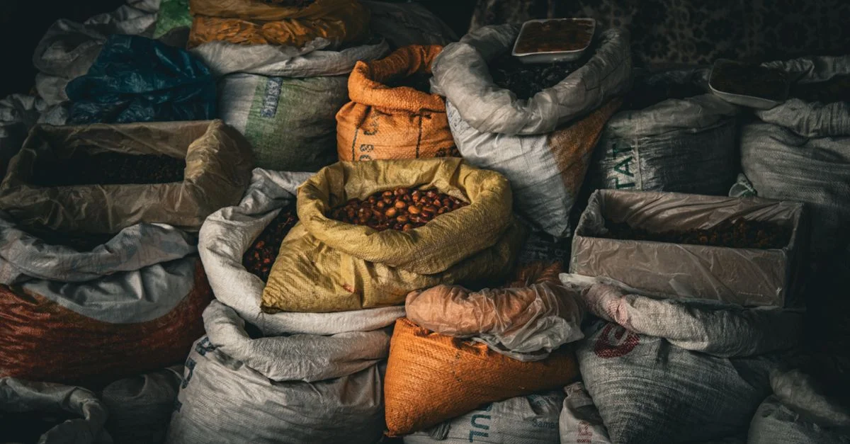 En un mercado cubierto, se exhibe una variedad de granos y especias en sacos de colores vivos, que ofrecen texturas exquisitas.