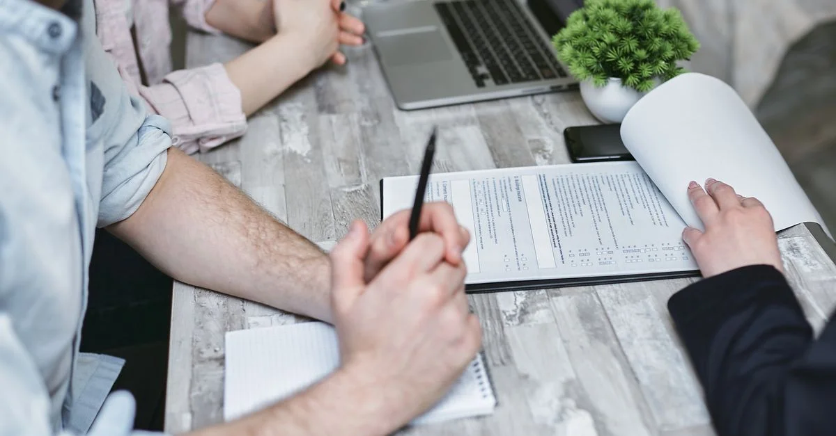 Primer plano de una reunión de negocios con documentos y laptop sobre una mesa blanca.