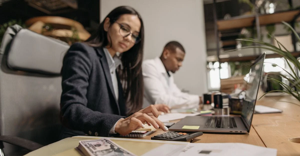 Dos profesionales de negocios colaborando con un portátil y una calculadora en una oficina moderna.
