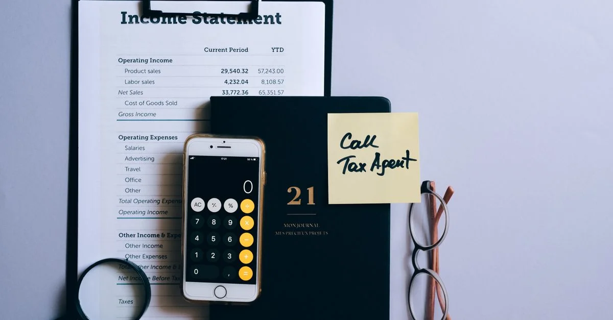 Vista superior de un escritorio con declaración de ingresos, calculadora de teléfono y nota de recordatorio de impuestos.