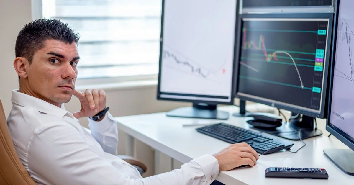 Analista profesional del mercado de valores monitorizando datos en múltiples pantallas en un puesto de trabajo.