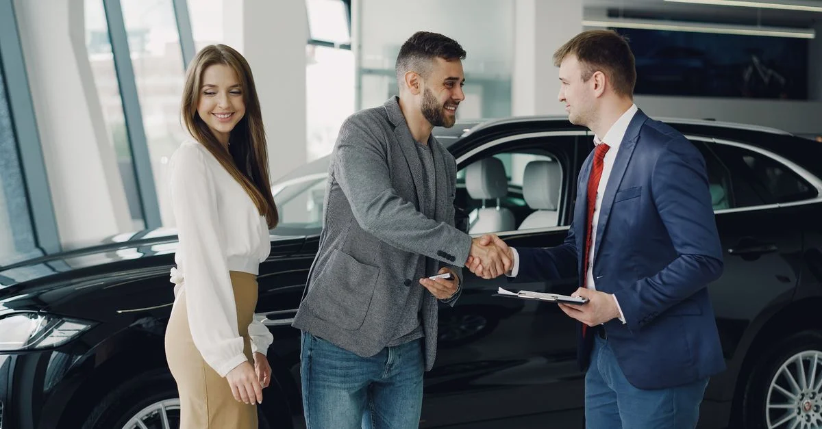 Compradores y vendedores se dan la mano en un concesionario de automóviles tras una compra exitosa.