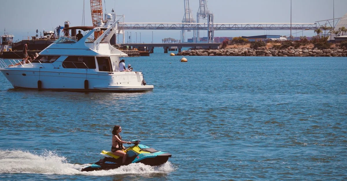 Escena recreativa en el puerto de Long Beach con una moto acuática y un yate bajo un cielo soleado.