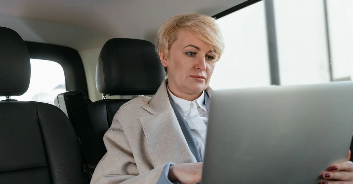 Mujer profesional con el pelo corto utilizando un portátil en el interior de un coche.