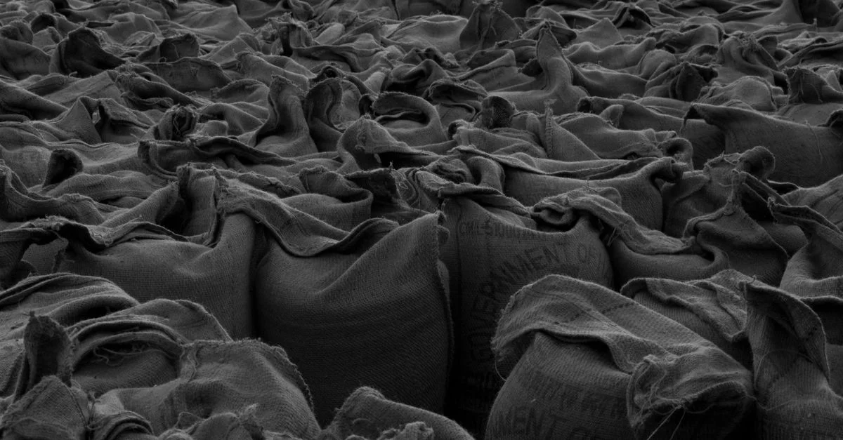Foto en monocromo de sacos de arpillera compactados, creando un patrón texturizado.