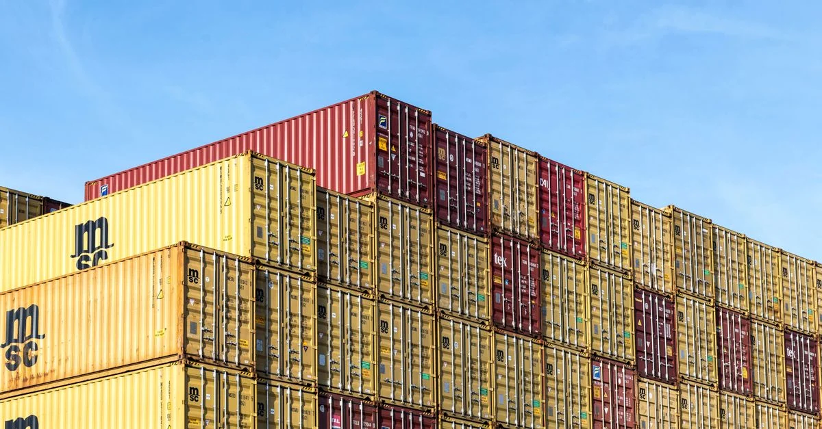 Contenedores de carga apilados y coloridos en el puerto de Hamburgo bajo un cielo azul claro.