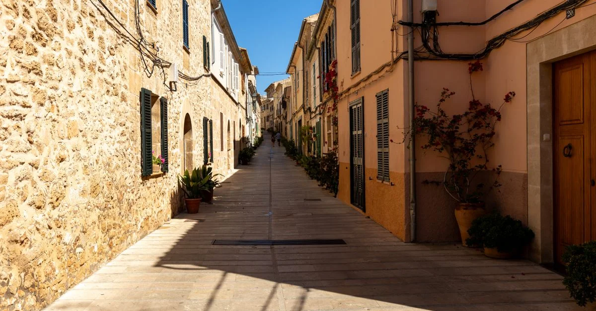 Encantador callejón angosto en Palma, Mallorca, rodeado de edificios rústicos de piedra bajo cielos azules.