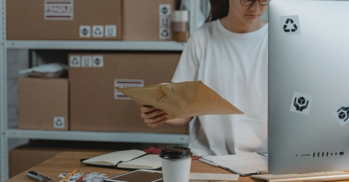 Mujer clasificando paquetes en su escritorio en una oficina de logística, mostrando una organización eficiente del espacio de trabajo.