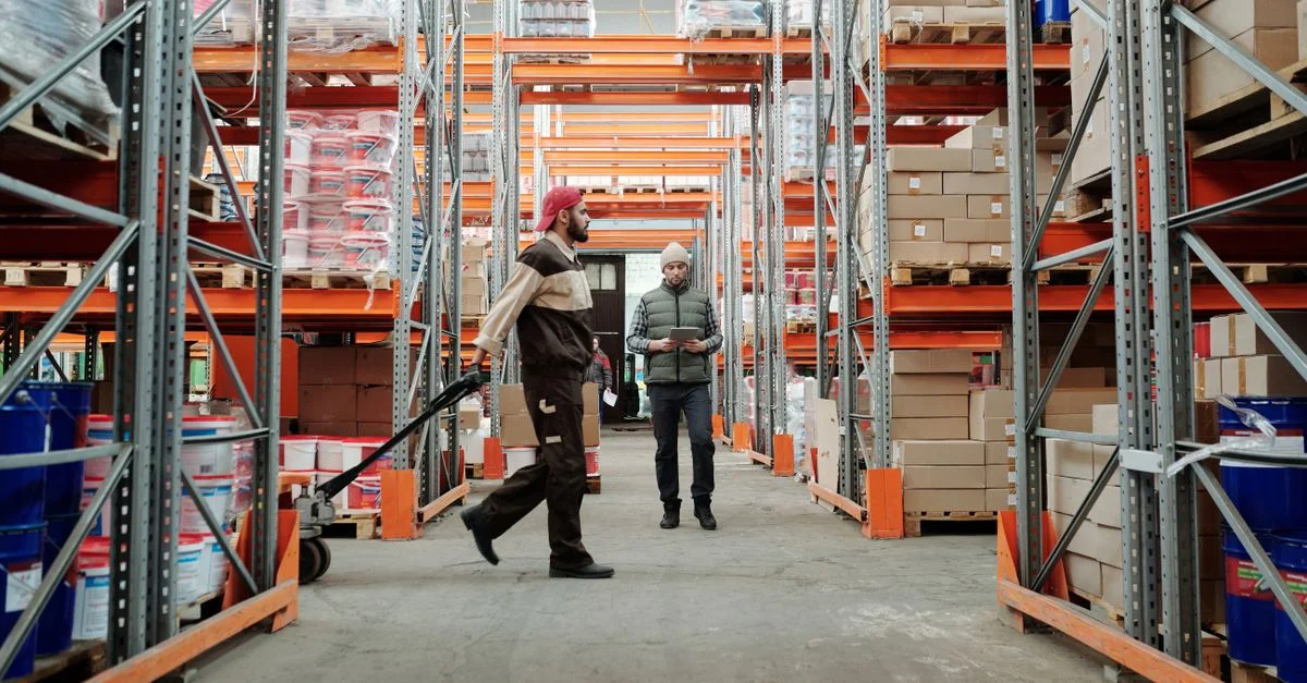 Dos trabajadores gestionan el inventario en un amplio pasillo del almacén.