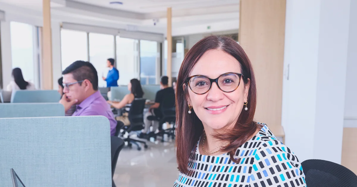 Mujer segura de sí misma en una oficina vibrante, resaltando el trabajo en equipo y la productividad.
