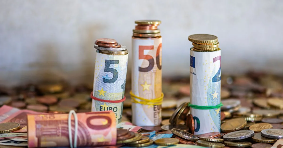 Primer plano de billetes y monedas de euro enrollados sobre una mesa, que simbolizan las finanzas y el ahorro.