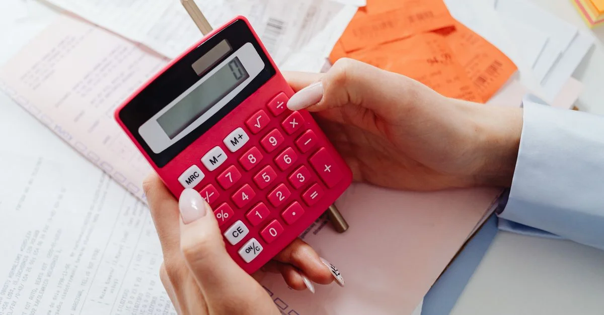 Primer plano de manos sosteniendo una calculadora roja, gestionando finanzas con documentos y recibos.
