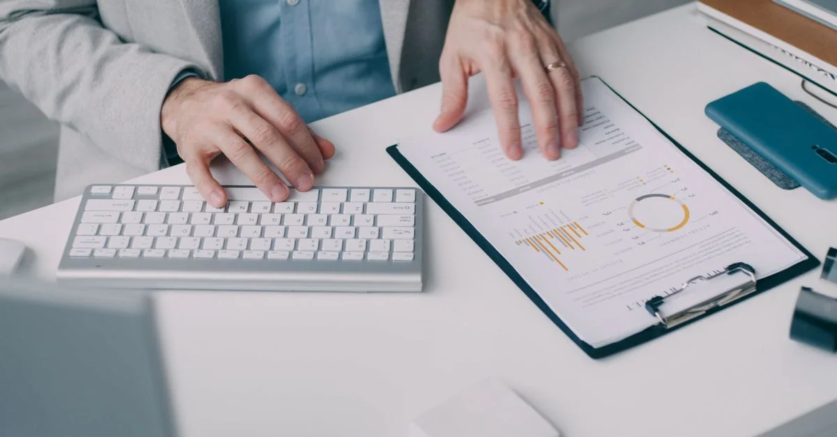 Un hombre trabajando con un informe financiero y un teclado en un entorno de oficina.