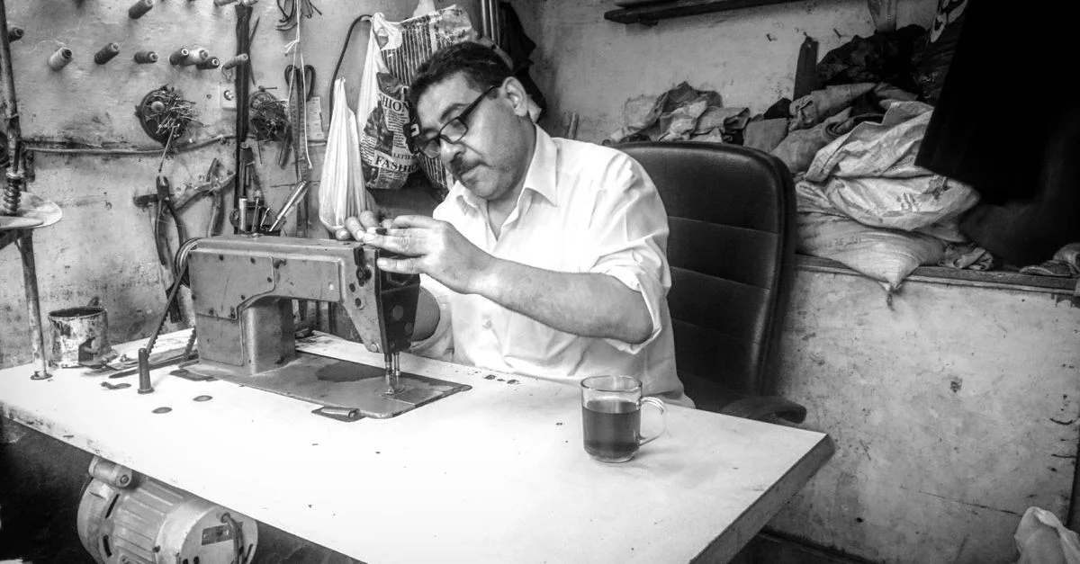 Imagen en blanco y negro de un sastre concentrado en coser en un taller en El Cairo.
