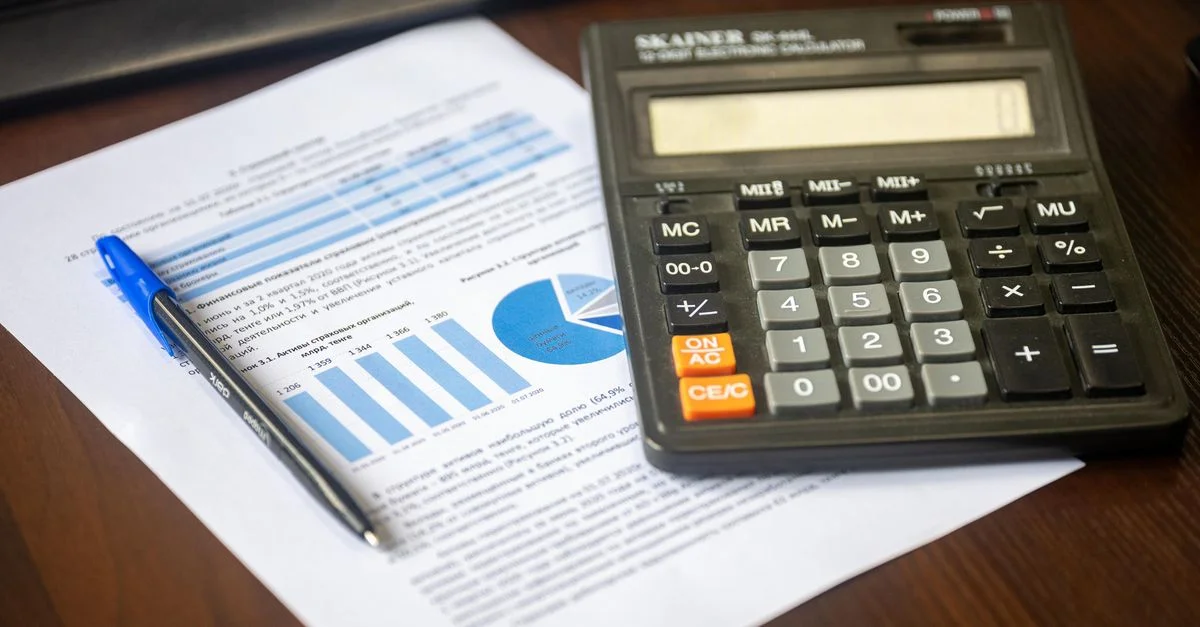 Primer plano de una calculadora, un bolígrafo y un informe financiero sobre un escritorio de madera.