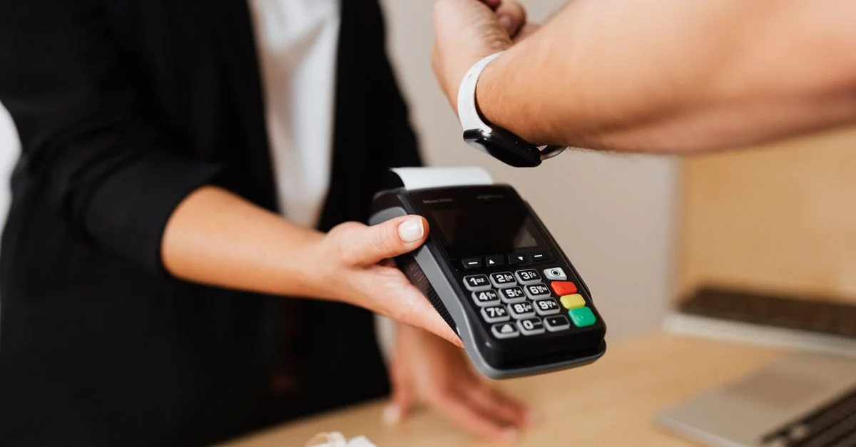 Persona realizando un pago sin contacto usando un reloj inteligente y un terminal de pago.