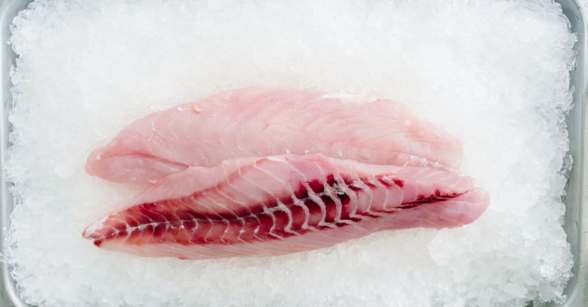 Close-up de filetes de pescado frescos y crudos colocados sobre una cama de hielo, mostrando su frescura.