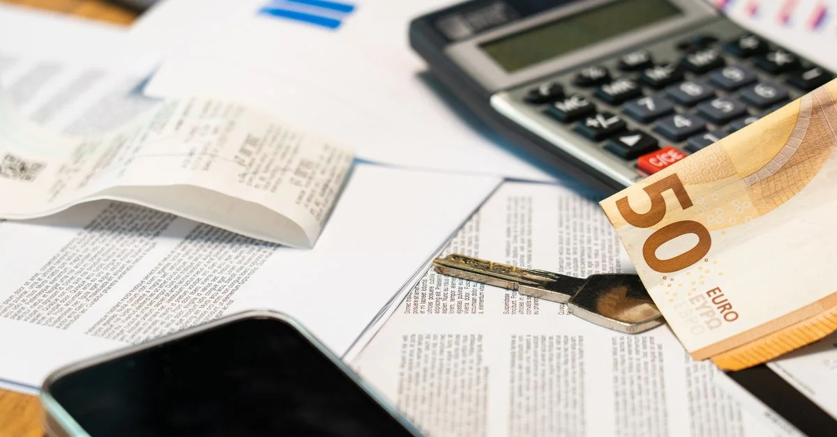 Vista plana de documentos financieros, billete de euro, calculadora, smartphone y llave para la gestión del presupuesto.