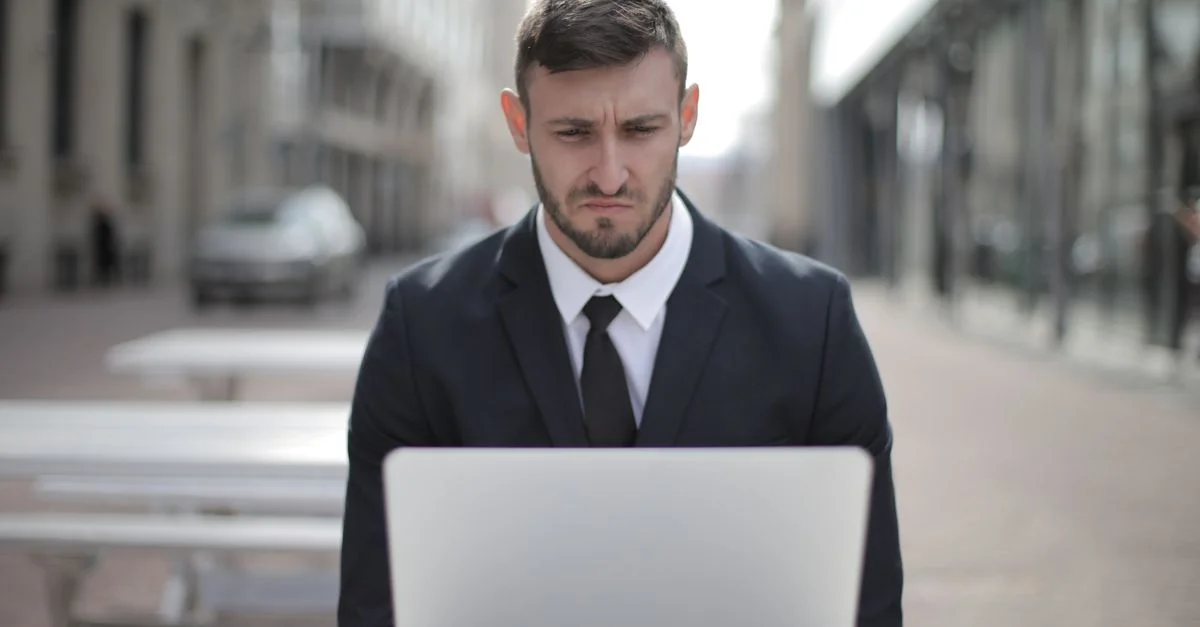 Un empresario concentrado en un traje trabaja en su computadora portátil al aire libre en un entorno urbano.