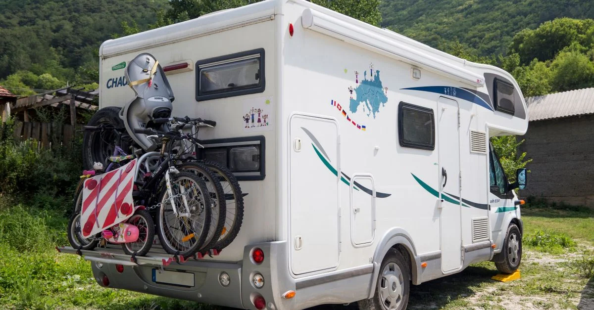 Una autocaravana con bicicletas acopladas en un entorno escénico al aire libre, rodeada de montañas y vegetación.