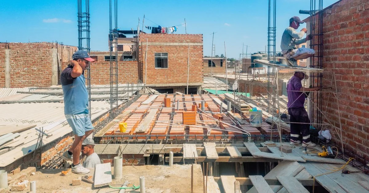 Obreros de la construcción levantando una estructura en Lambayeque, Perú, bajo un cielo azul despejado.