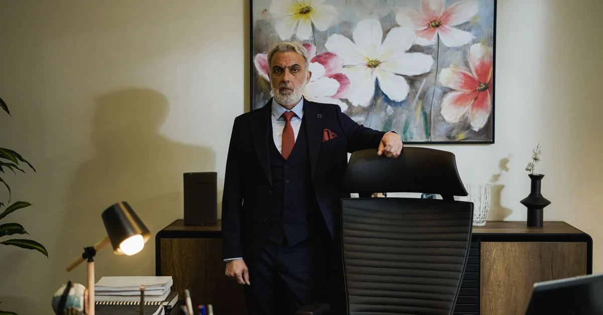 Distinguido empresario maduro en traje, de pie con confianza en una oficina moderna.