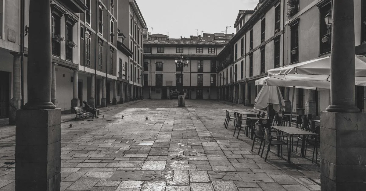 Vista en blanco y negro de una plaza histórica con mesas de café vacías en Oviedo, España.