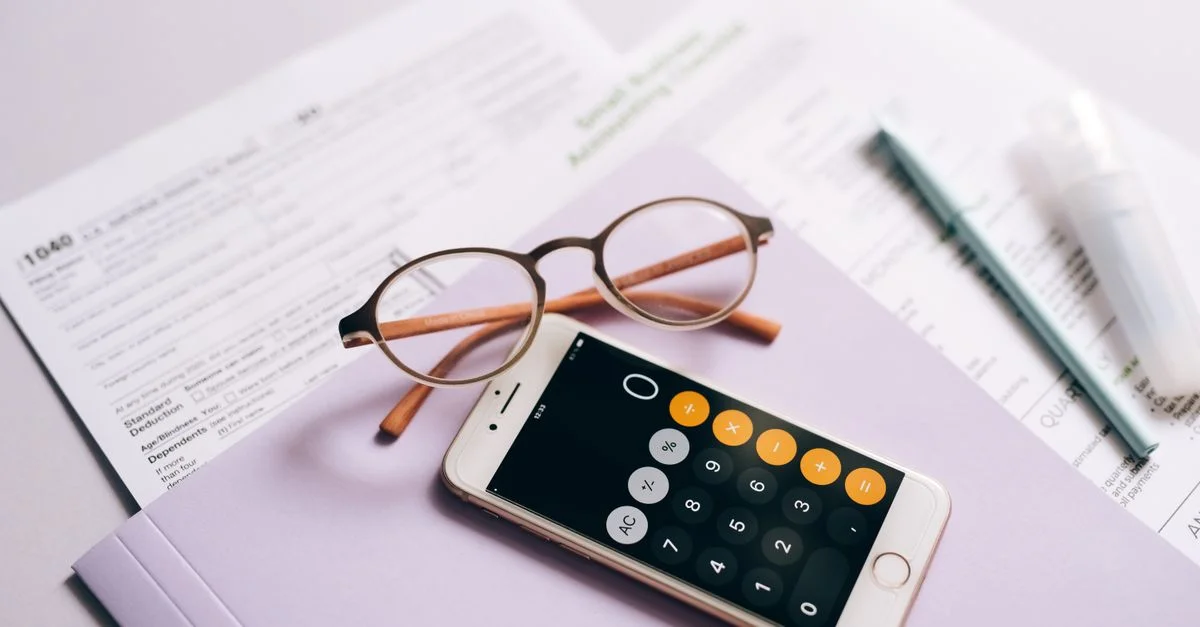 Un calculador de smartphone y gafas sobre documentos fiscales, representando la preparación moderna de impuestos.