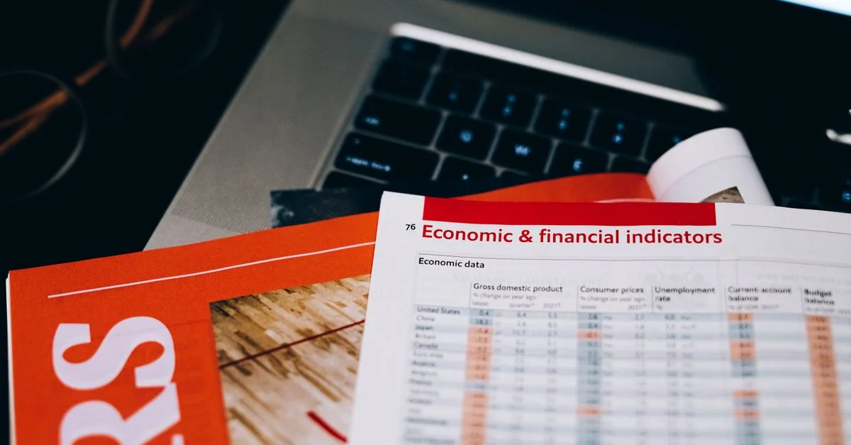 Primer plano detallado de documentos económicos y financieros sobre un teclado de portátil, destacando el análisis de datos.