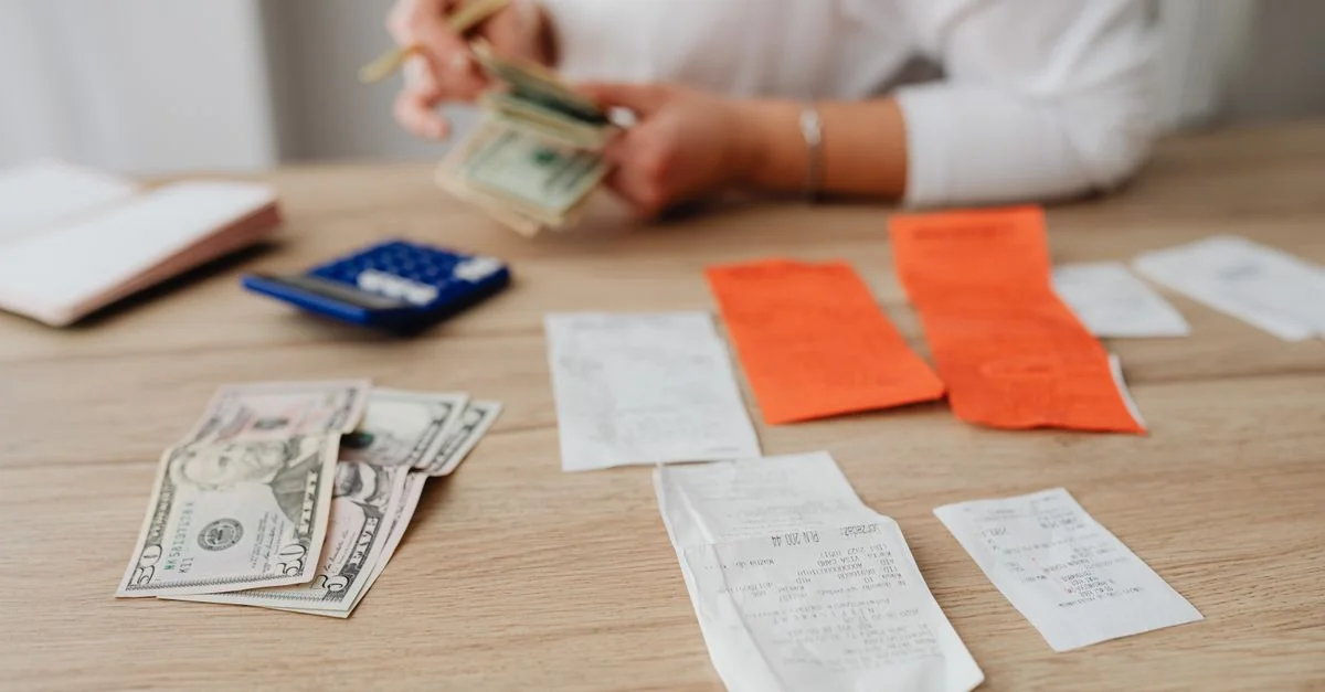 Una persona usando una calculadora y efectivo para planificar un presupuesto doméstico.
