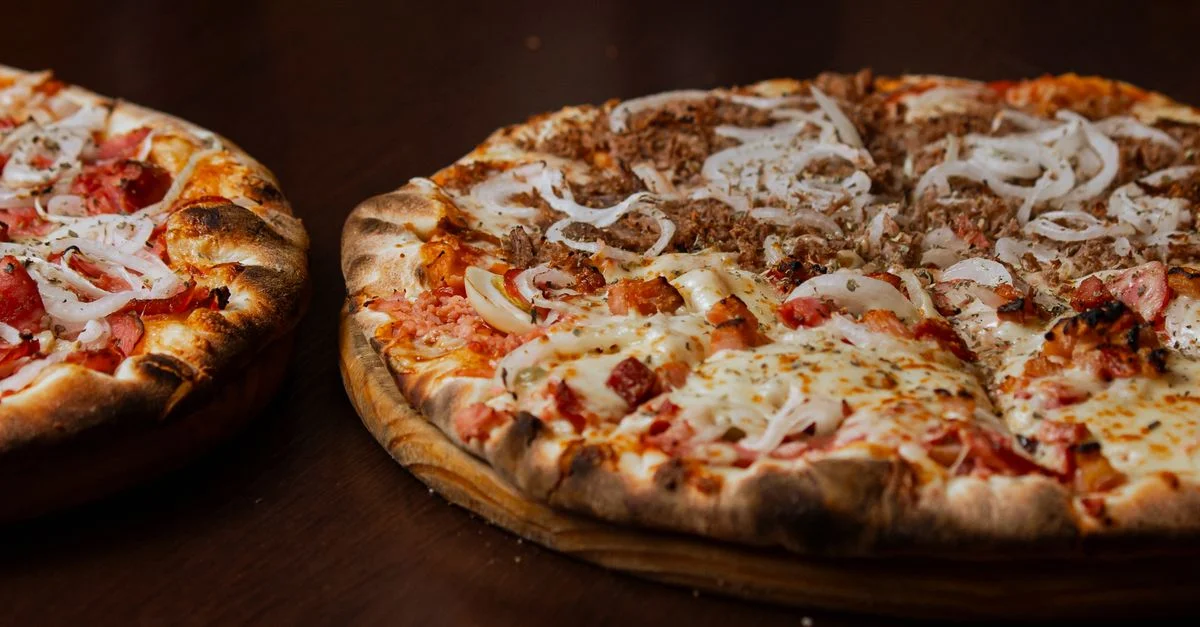 Primer plano de dos deliciosas pizzas con pepperoni y cebolla en una mesa de madera.