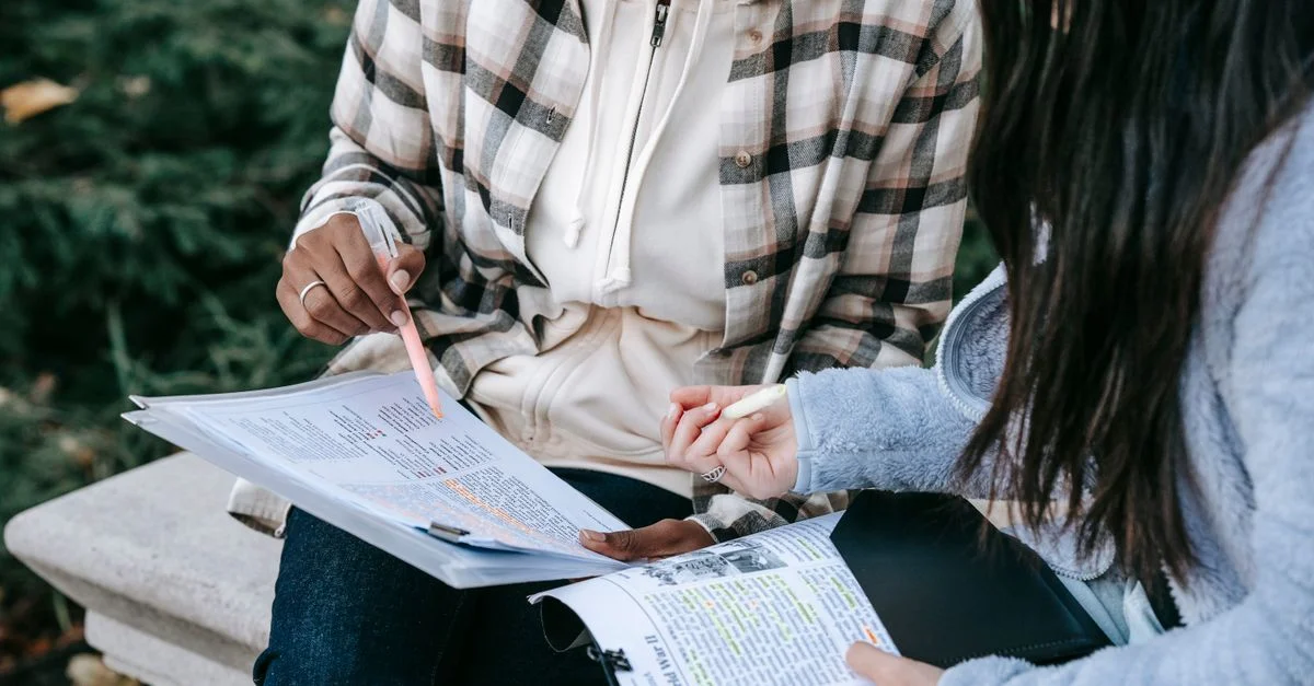 Dos estudiantes universitarios colaborando en un proyecto, destacando el trabajo en equipo y la educación en un entorno al aire libre.