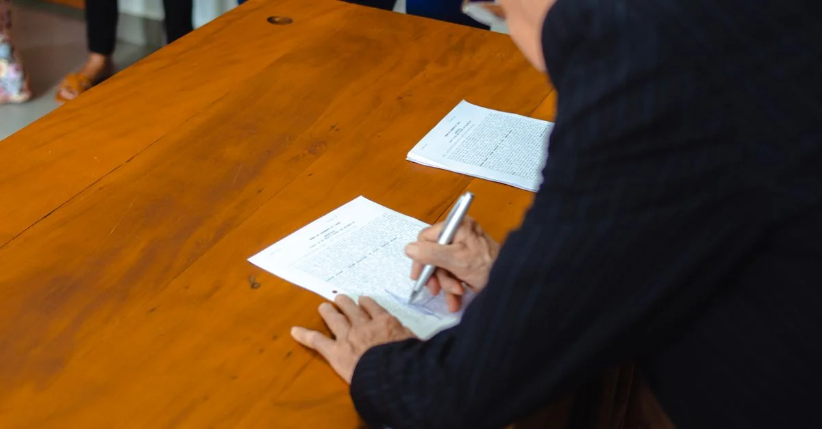 Un primer plano de un empresario firmando documentos oficiales en un escritorio de madera.