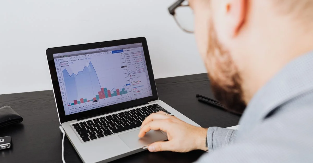 Hombre trabajando en un portátil analizando datos empresariales y gráficos financieros en interiores.